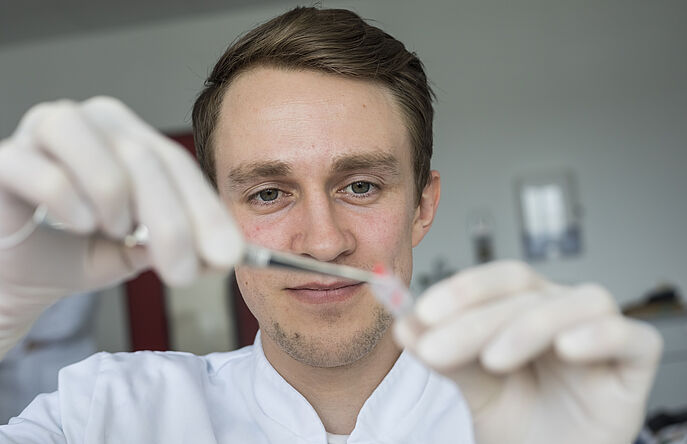 Lab tech wearing gloves and holding tweezers and vial with cotton