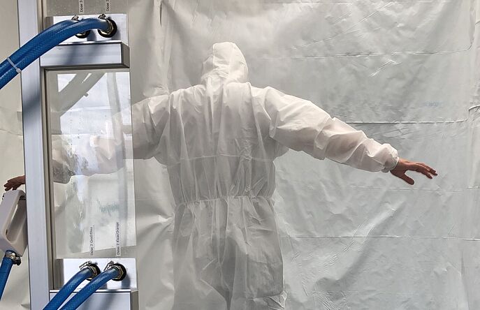 Man wearing white PPE suit in testing chamber during spray test