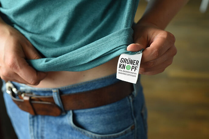 Green Button Certification and Label for Sustainable Textiles Person in green t-shirt showing green button sew-in label