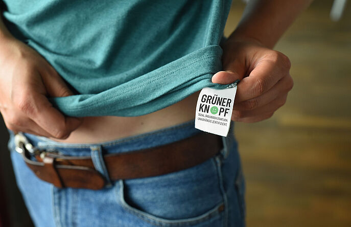 Green Button Certification and Label for Sustainable Textiles Person in green t-shirt showing green button sew-in label