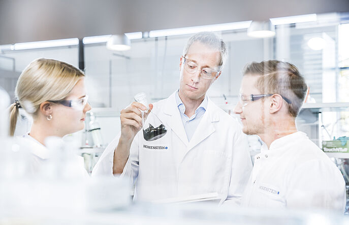 3 chemists holding textile chemicals in beaker