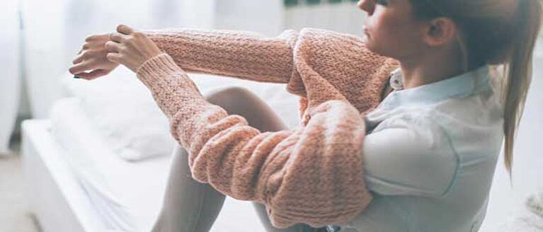 Woman putting on a sweater while sitting on a bed