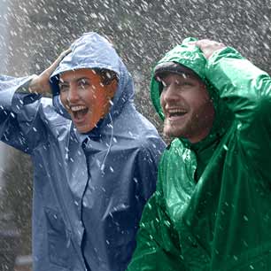 Woman in blue raincoat and man in green raincoat, shielding themselves from heavy rain