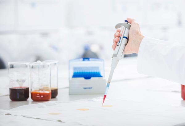 Lab technician hand dropping colored liquids on fabric with pipette