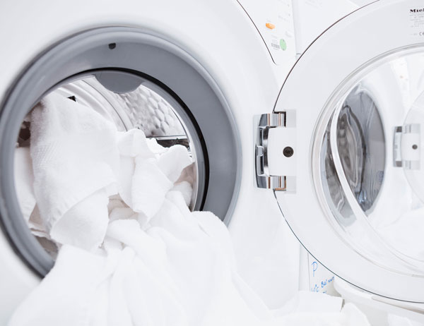 Home laundry machine with door open and white linens