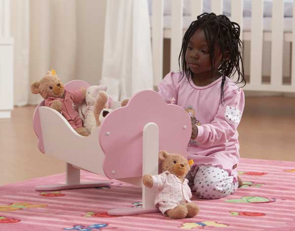 Young child wearing pink clothes, sitting on a rug with a cradle and dolls