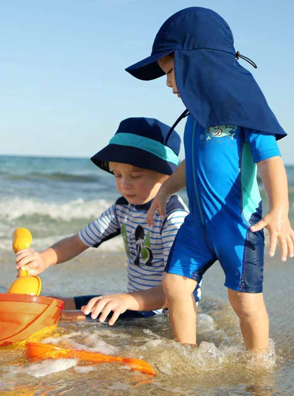 two kids wearing UV protective clothing, playing on a sunny beach